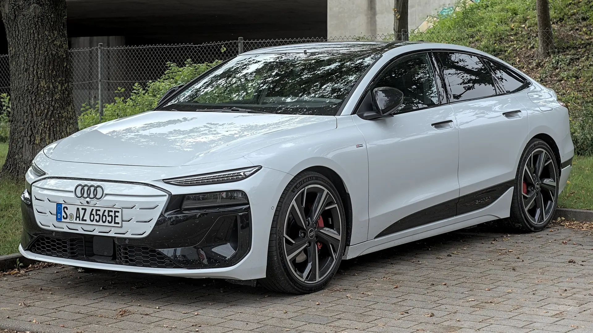 Een witte Audi A6 Sportback e-tron, schuin van voren gezien, geparkeerd op een klinkerstrook onder een betonnen viaduct