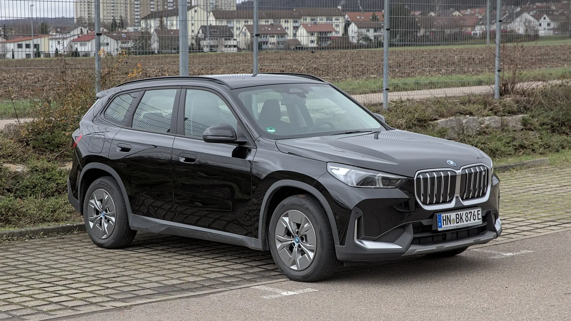 Een zwarte BMW iX1, schuin van voren, op een parkeerplaats