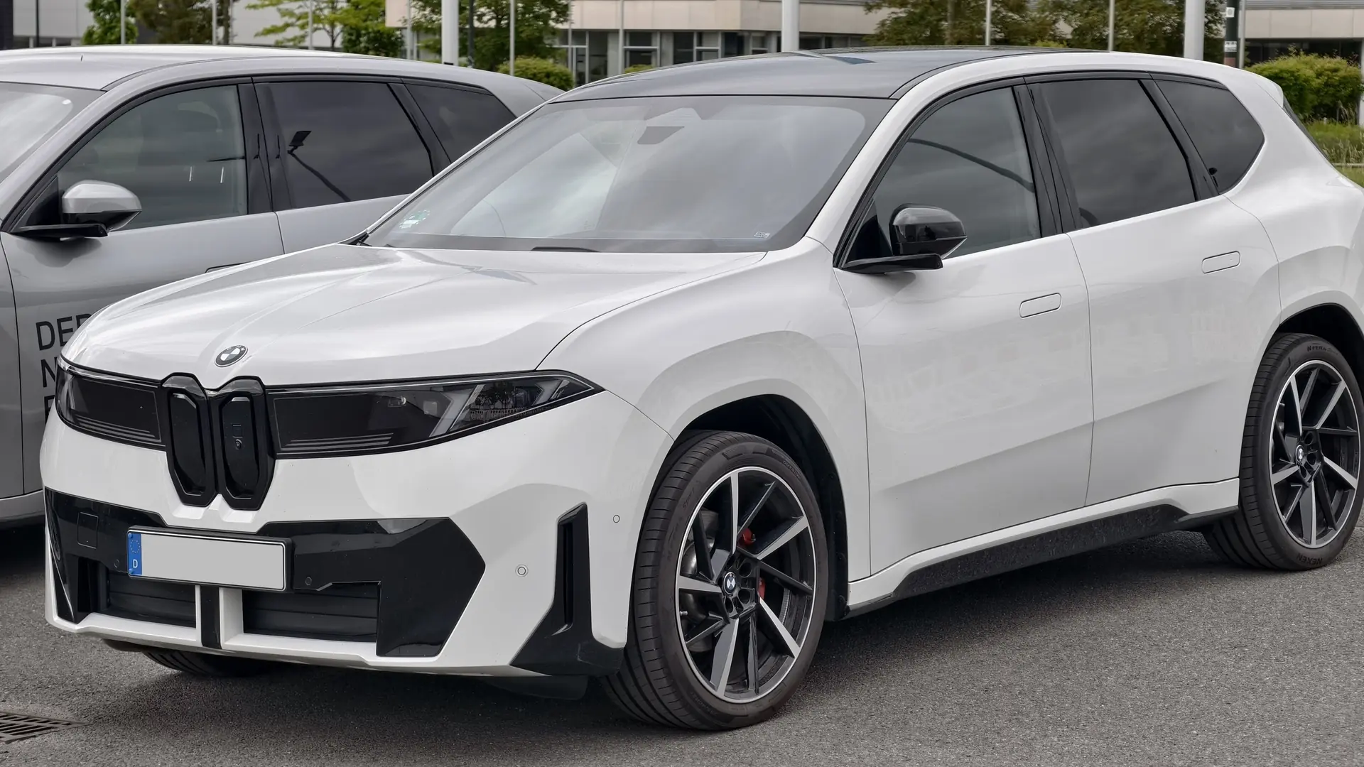 Een witte BMW iX3 van de nieuwe generatie, schuin van voren, op een parkeerplaats