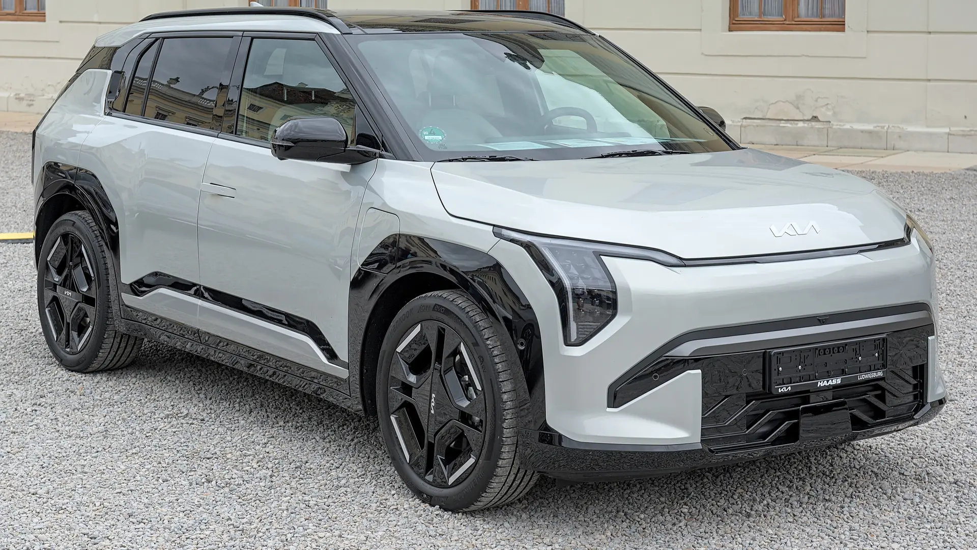 Een zilvergrijze Kia EV3 GT-Line, schuin van voren, op een plein voor een gebouw