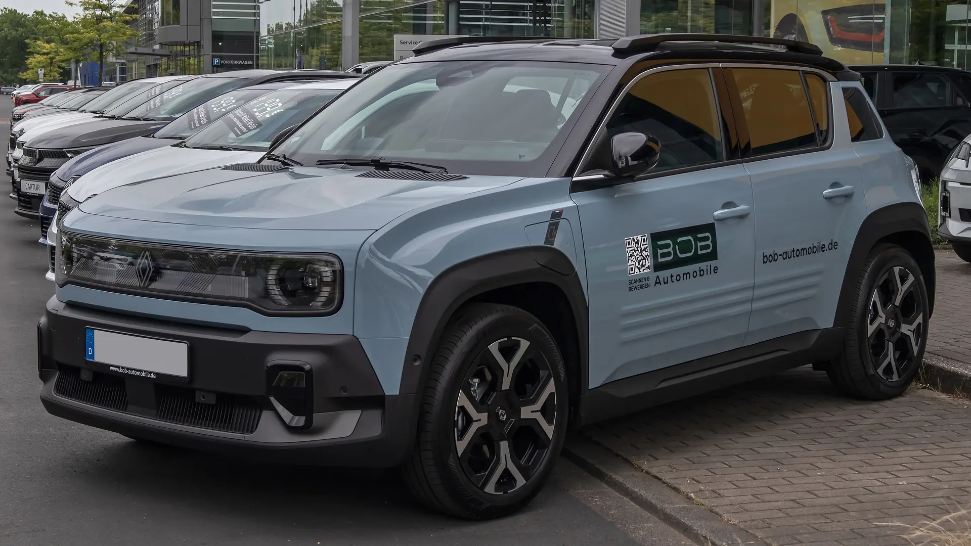 Een grijsblauwe Renault 4 E-Tech electric, schuin van voren, op een parkeerplaats