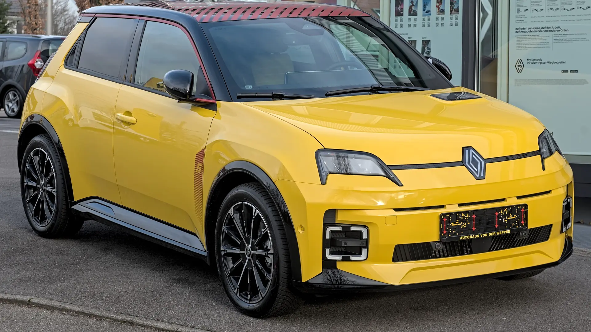 Een gele Renault 5 E-Tech electric, schuin van voren, bij een showroom