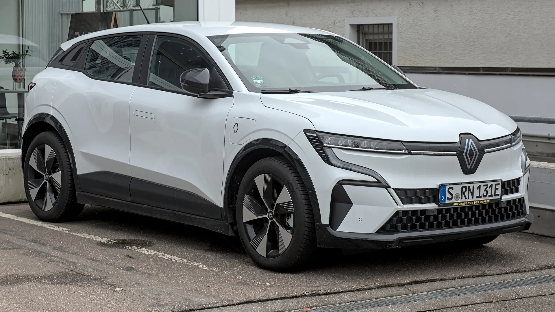 Een witte Renault Megane E-Tech electric, schuin van voren, bij een showroom