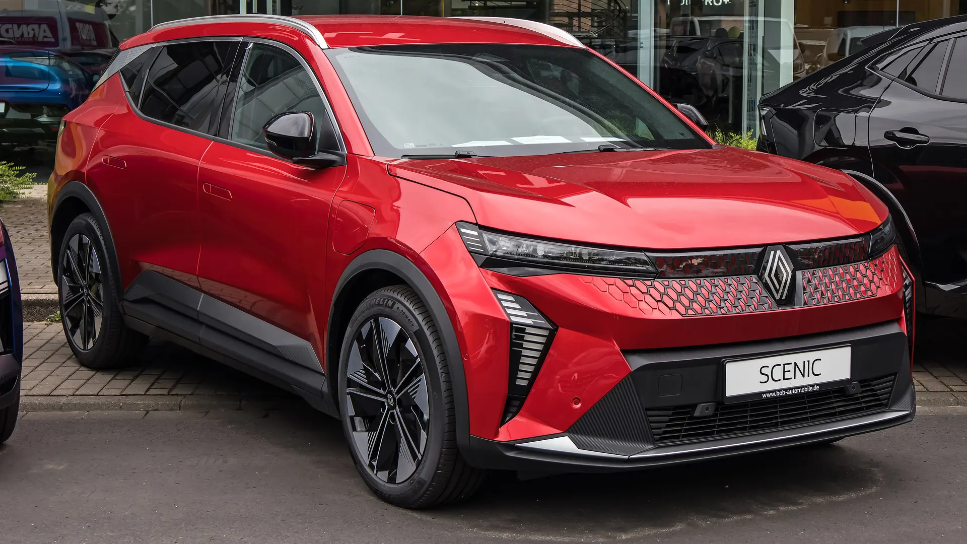Een rode Renault Scenic E-Tech electric, schuin van voren, bij een showroom