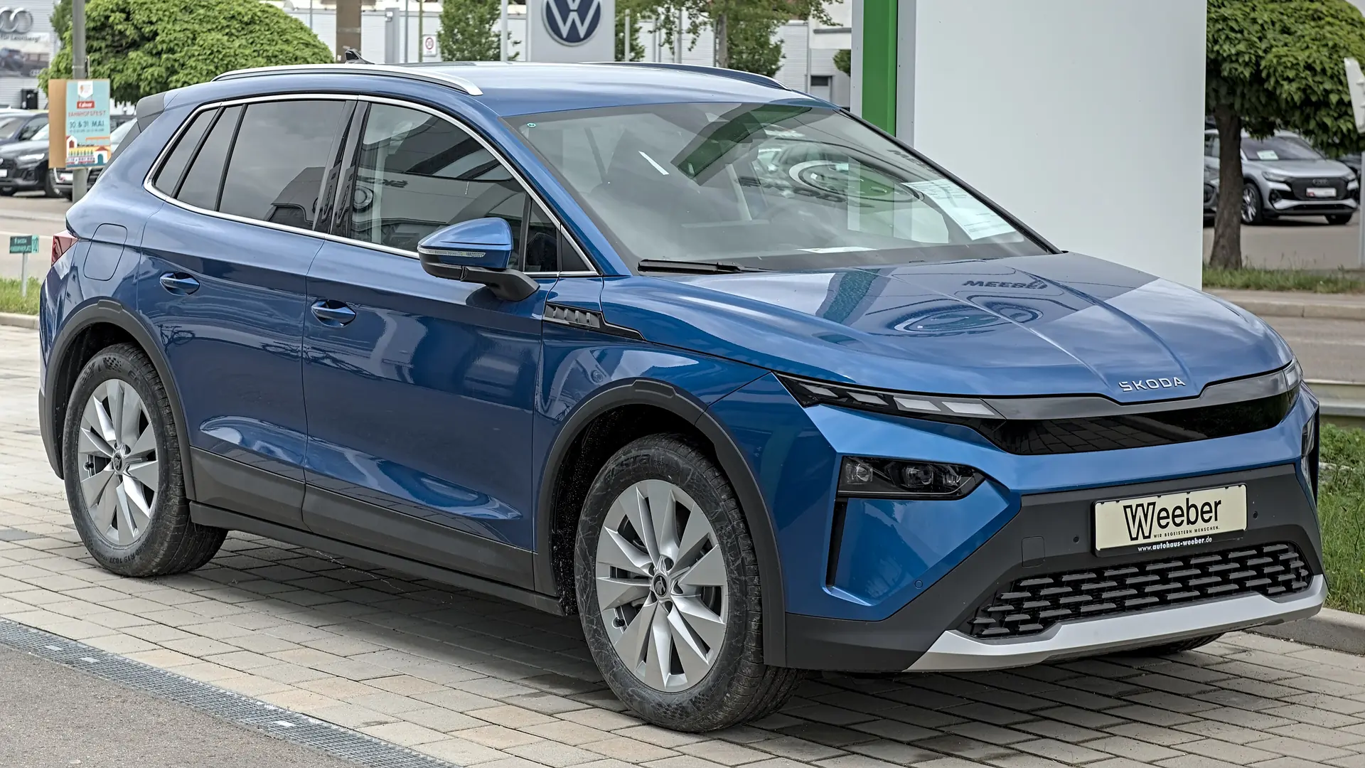 Een blauwe Škoda Elroq, schuin van voren, bij een showroom