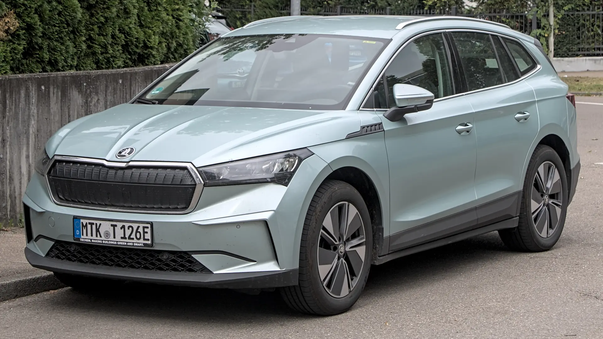 Een lichtgroene Škoda Enyaq, schuin van voren, geparkeerd langs een muur